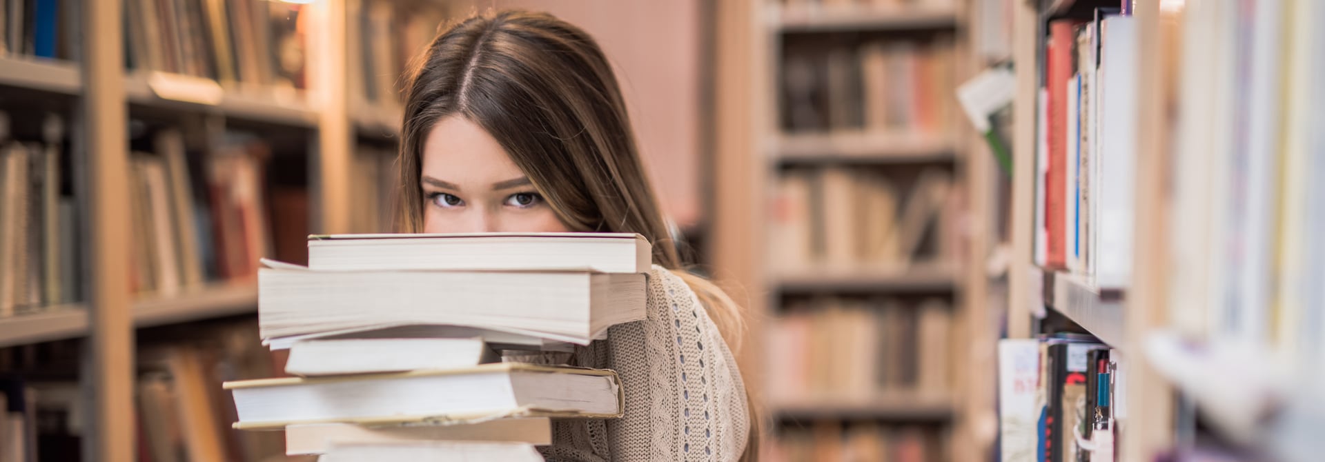 Mädchen versteckt sich hinter einem Stapel Bücher