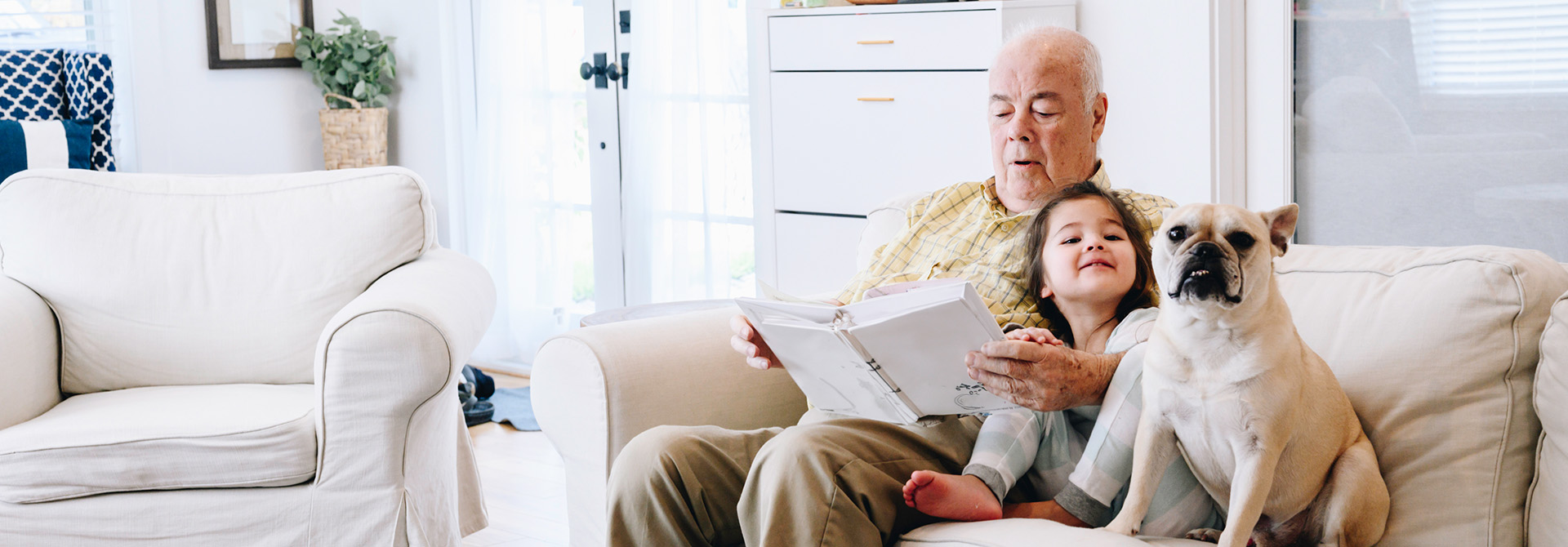 Opa und Kind Älterer Mann und Kind sitzen auf einem Sofa, der Mann hält ein Buch, ein Hund sitzt neben ihnen